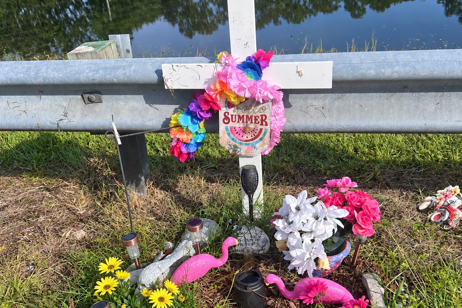 White roadside memorial cross decorated with colorful flowers and a Summer sign